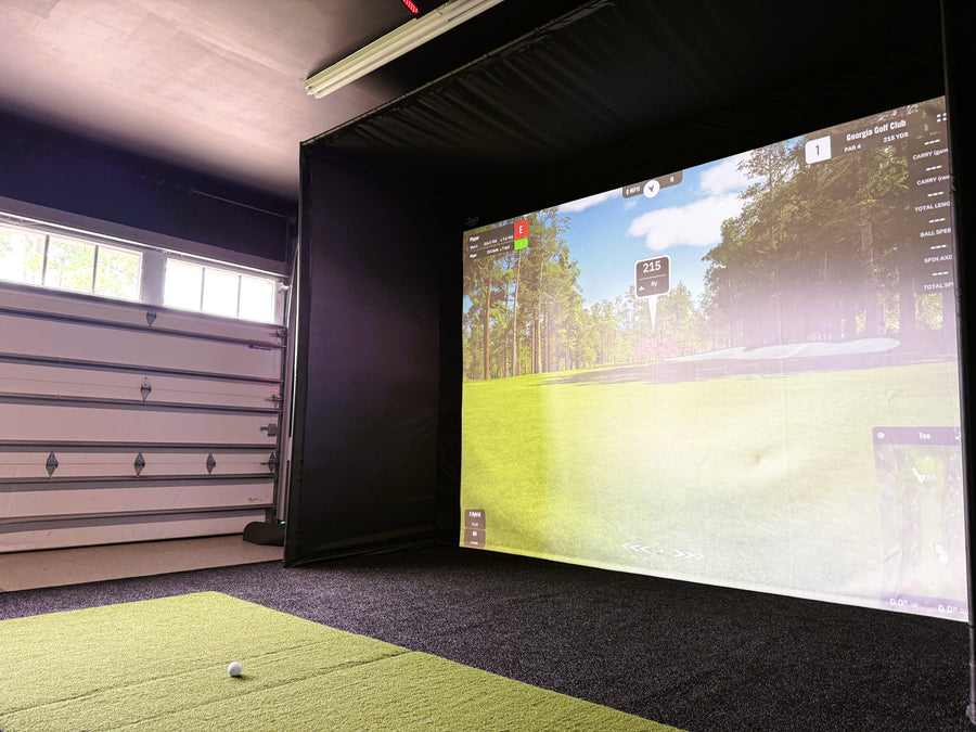 Indoor golf simulator setup in a garage with a screen displaying a golf course.