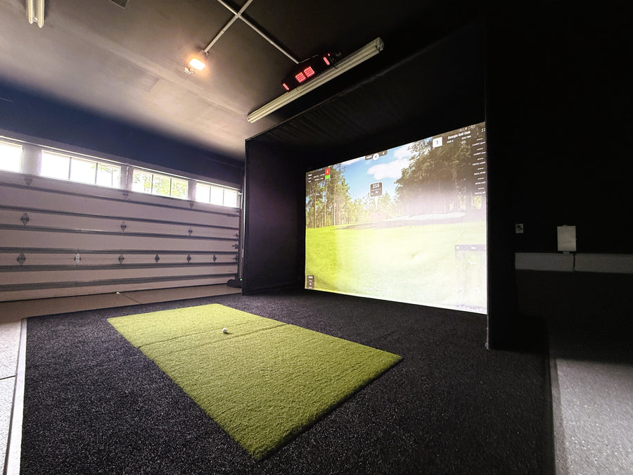 Indoor golf simulator setup in a garage with a screen displaying a golf course.