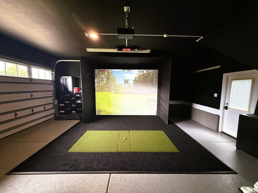 Indoor golf simulator setup in a garage with a screen displaying a golf course.