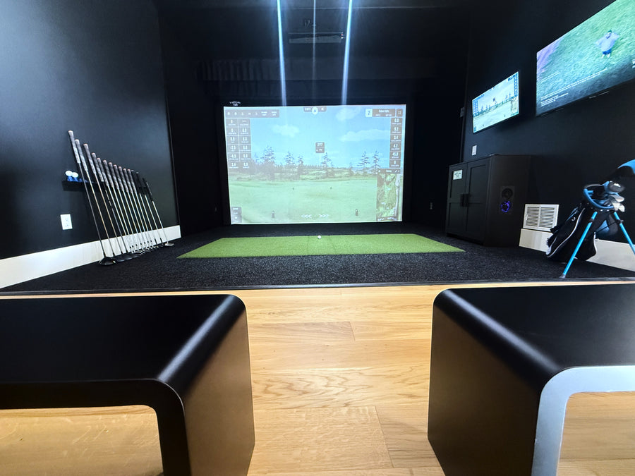 Golf simulator setup in a room with multiple screens and golf clubs.