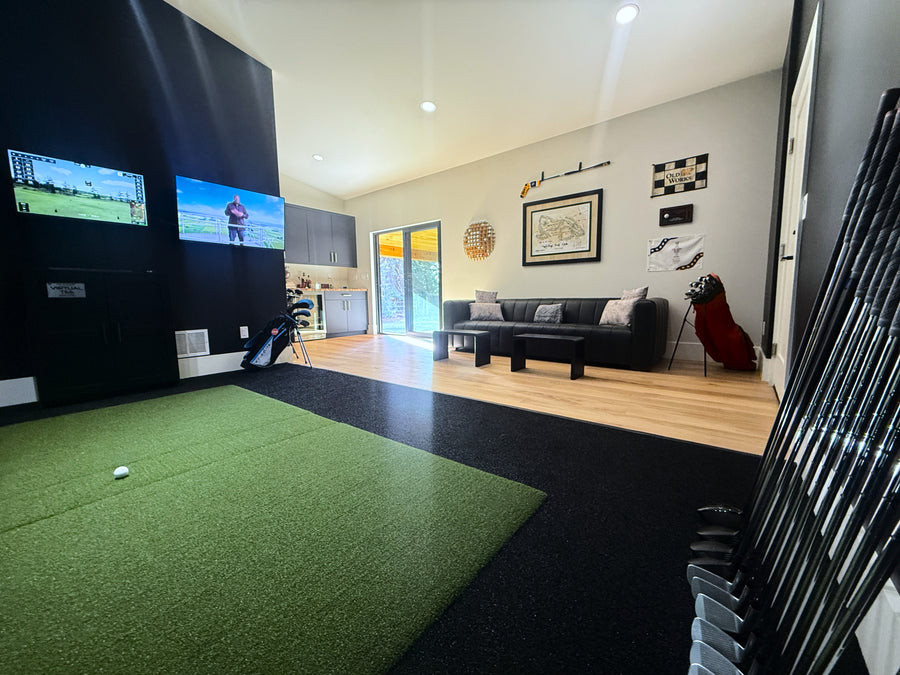 Golf simulator setup in a living room with green turf area and TV screens.