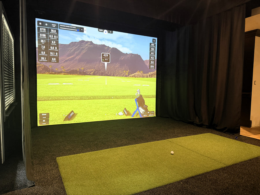 Indoor golf simulator setup with screen displaying a golf course and green mat on the floor.