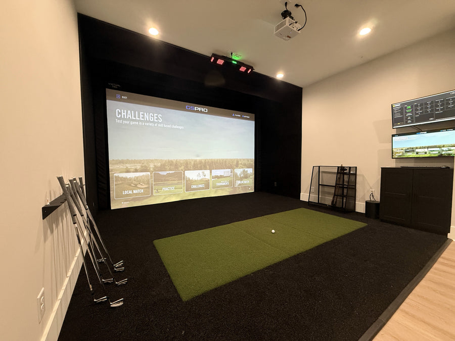 Indoor golf simulator setup with screen displaying a golf course and various equipment.