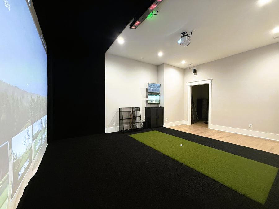 Indoor golf simulator setup with projection screen and green mat on wooden floor.