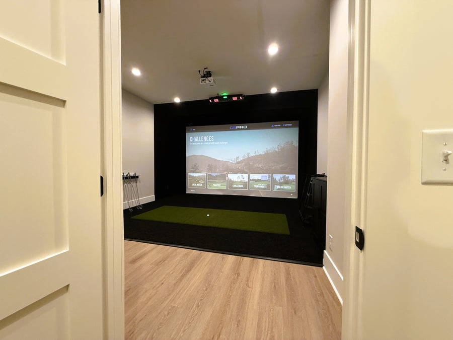 Indoor golf simulator setup in a room with a screen displaying a golf course.