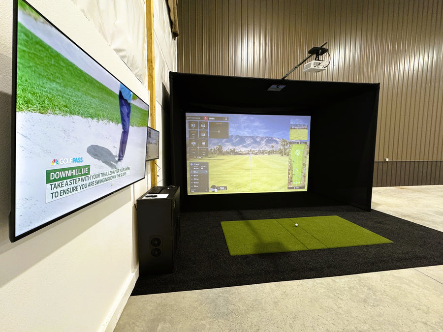Golf simulator setup with two screens displaying a golf course and a green mat on the floor.