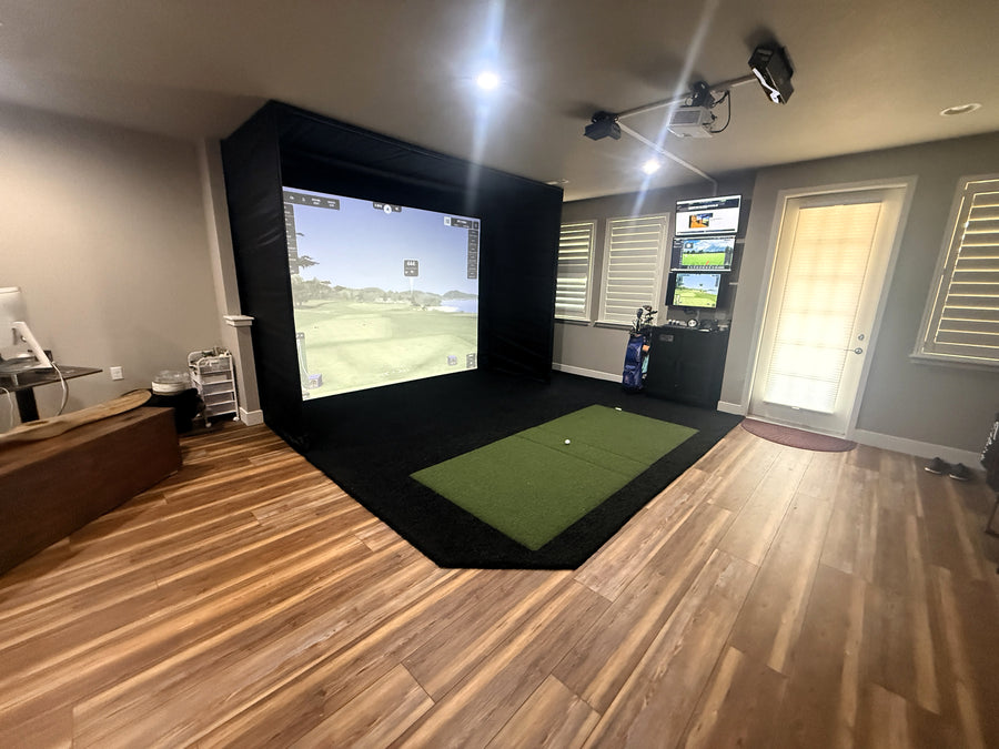 Indoor golf simulator setup in a room with wooden flooring and a large screen displaying a golf course.