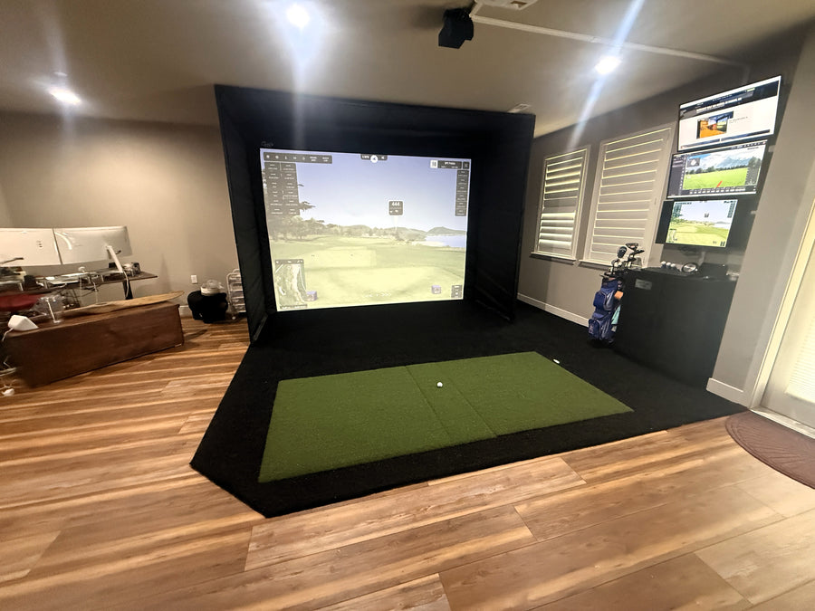 Golf simulator setup in a room with multiple screens and golf equipment.