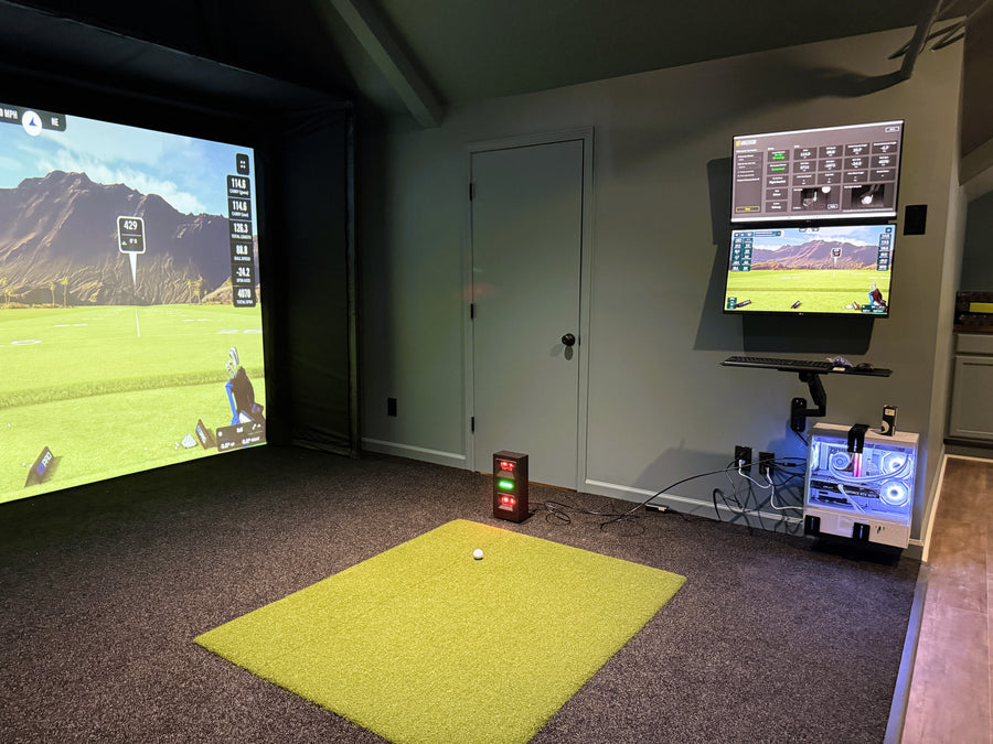 Golf simulator setup in a room with two screens displaying a golf course.