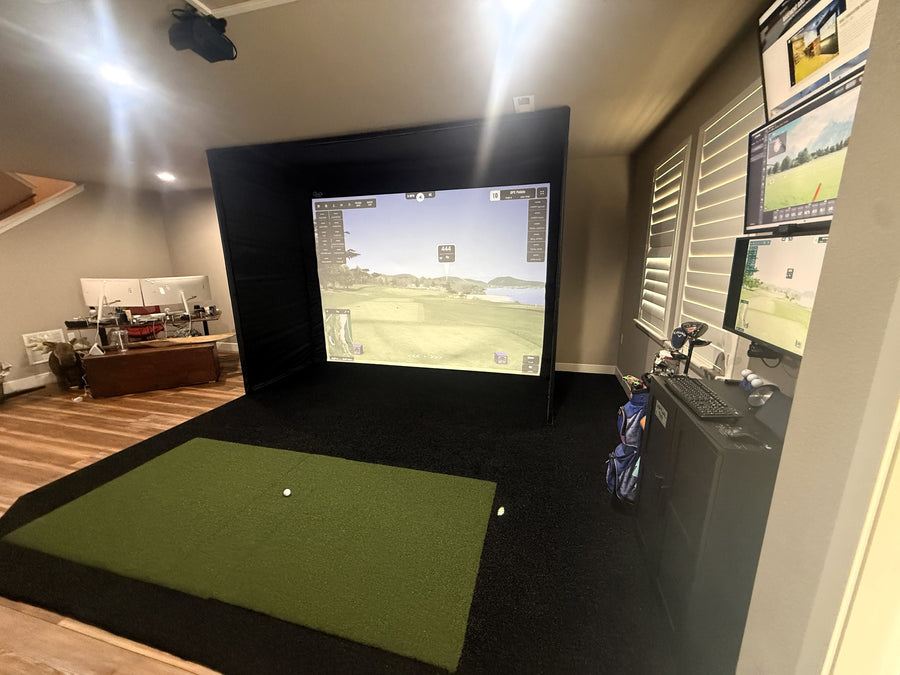 Indoor golf simulator setup with multiple screens and a green mat.