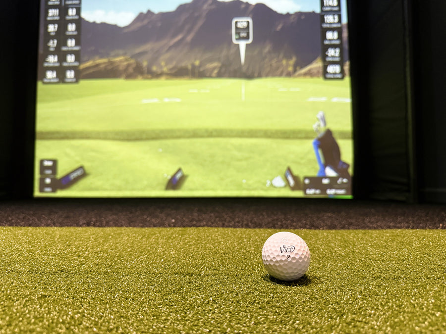 Golf ball on a golf simulator screen displaying a golf course with mountains in the background.