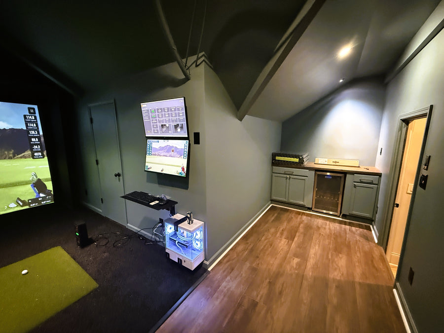 Indoor golf simulator setup with multiple screens and a small device on a stand.