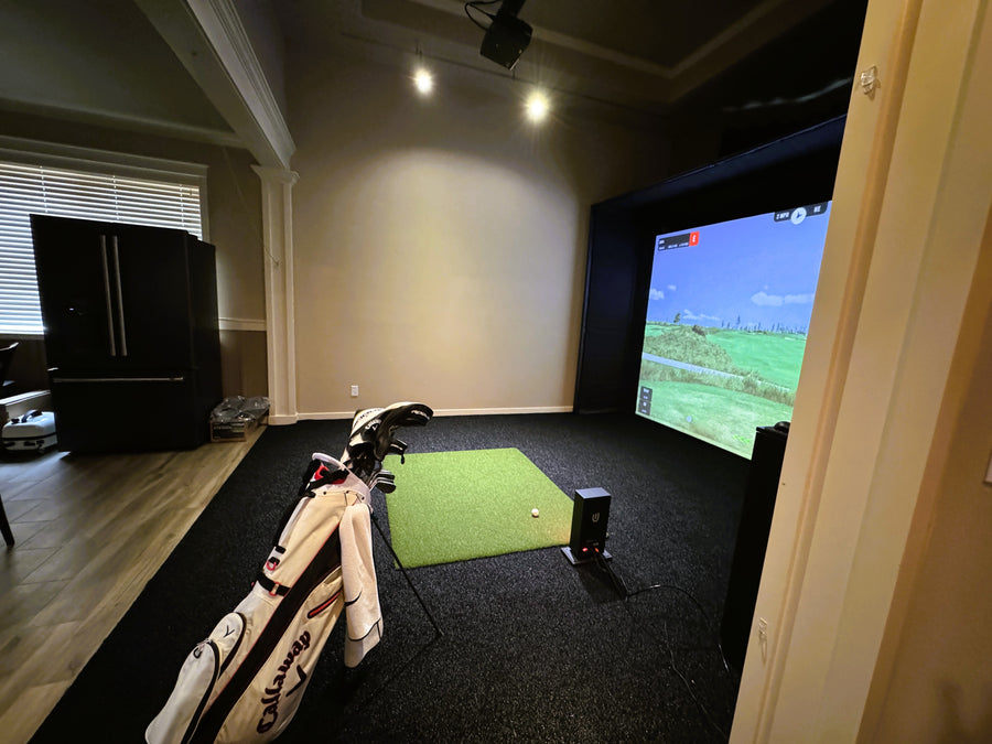 Golf simulator setup in a home room with a screen displaying a golf course.