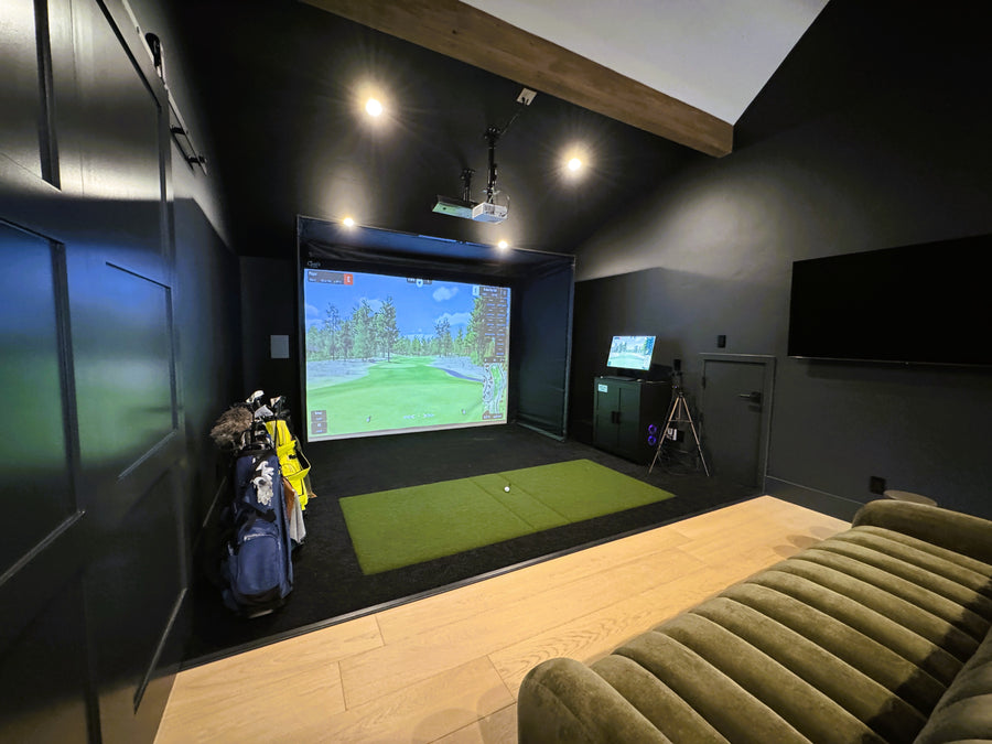 Indoor golf simulator setup in a room with a couch and golf equipment.