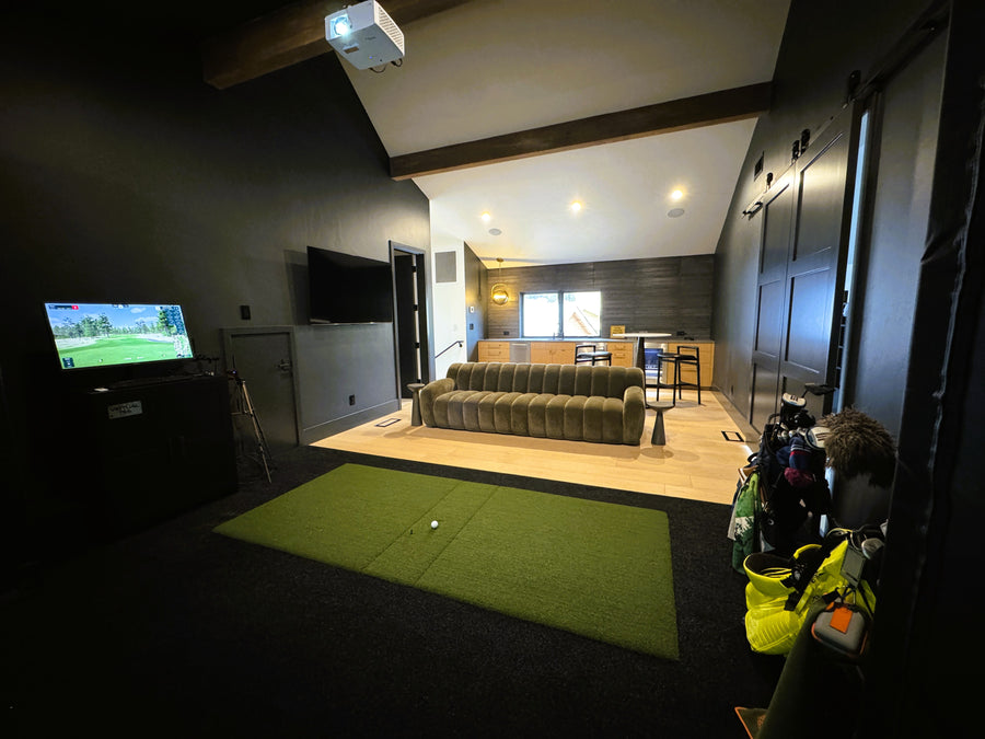 Indoor golf simulator setup in a room with a green mat and TV displaying a golf game.