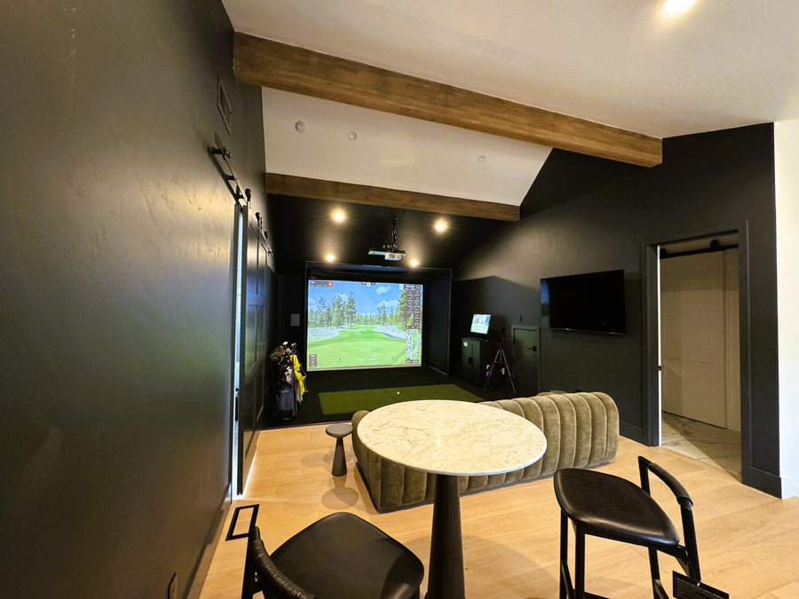 Modern golf simulator room with a large screen displaying a video game, surrounded by comfortable seating and decor.