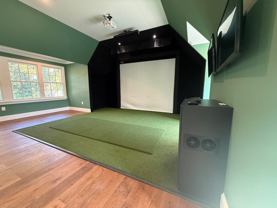 Indoor golf simulator setup with screen, projector, and speakers in a room with green walls and wooden floor.