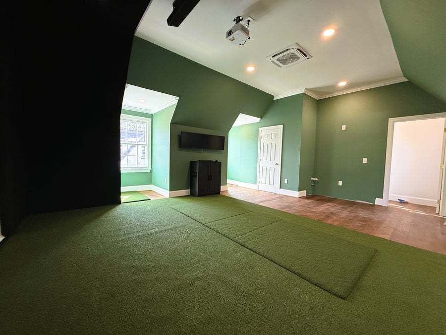 Golf simulator room with a large mat on the floor, white walls, and a door.