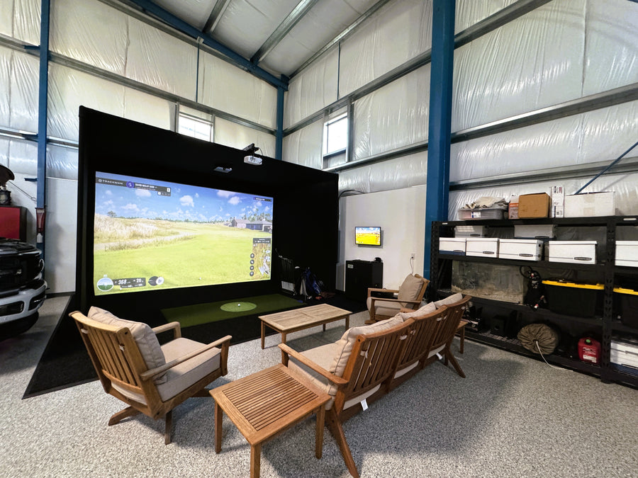 Indoor golf simulator with a large screen displaying a game, surrounded by comfortable seating and shelves.