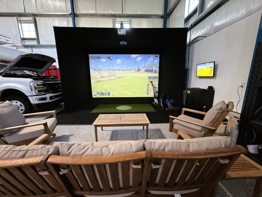 Indoor golf simulator area with a large screen displaying a game, surrounded by comfortable seating and a vehicle.
