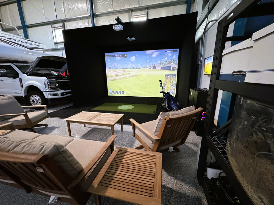 Indoor golf simulator area with a large screen displaying a golf game, surrounded by furniture and vehicles.