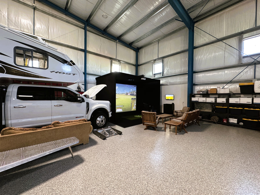 Indoor golf simulator in airplane hangar with RV, truck, and living quarters setup inside
