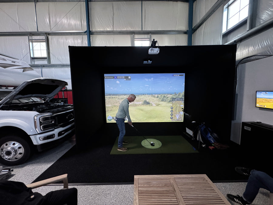 Indoor golf simulator game in a garage with a truck and equipment around.