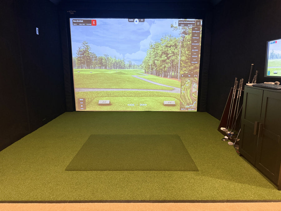Indoor golf simulator setup with green turf and screen displaying a golf course.