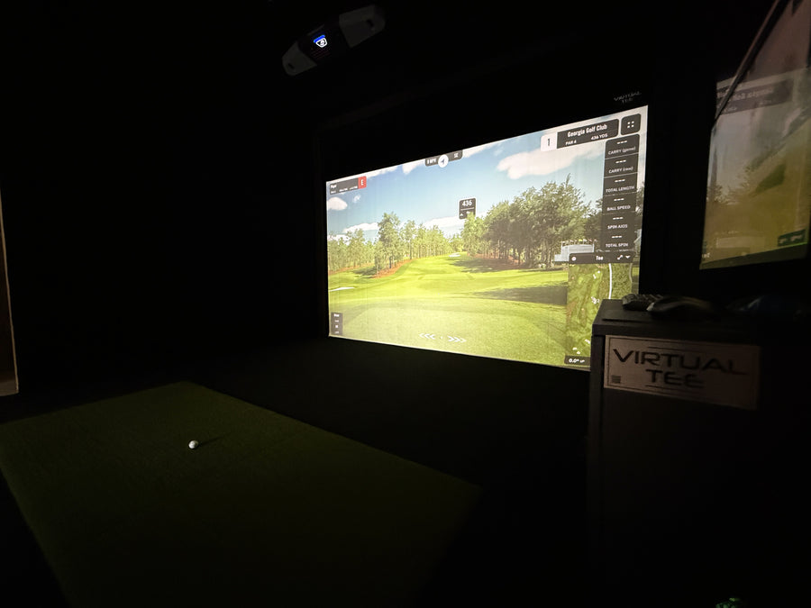 Golf simulator setup with screen displaying a golf course and 'Virtual Tee' branding.