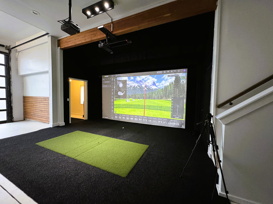 Indoor golf simulator setup in a room with a screen displaying a golf course.