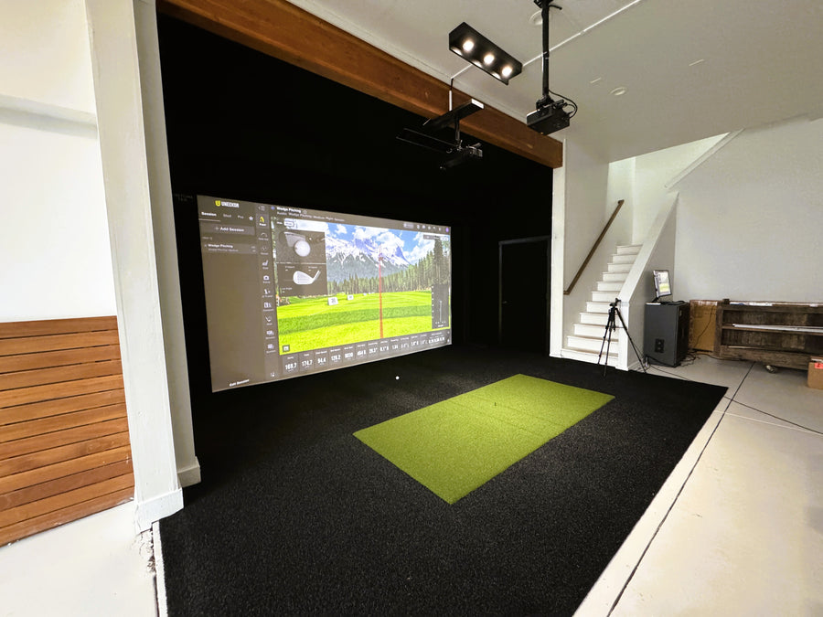 Indoor golf simulator setup with a screen displaying a golf course on a black floor.
