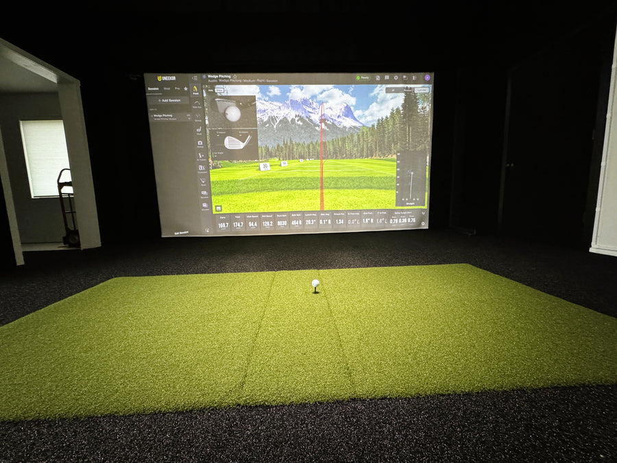 Golf simulator setup with screen displaying a golf course and a golf ball on a green floor.