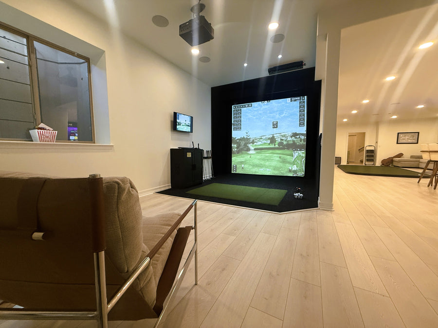 Indoor golf simulator setup in a living room with a couch and TV.