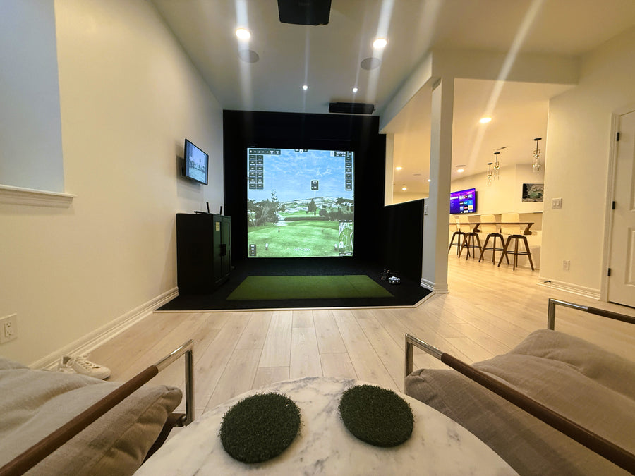 Indoor golf simulator setup in a modern living room with multiple screens.