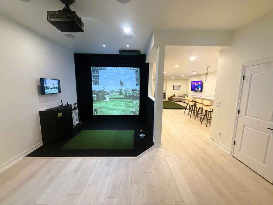 Indoor golf simulator setup in a modern living room with a projector screen and multiple televisions.