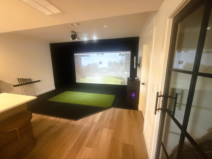 Indoor golf simulator setup in a room with a screen displaying a golf course.