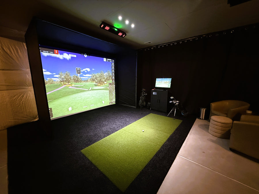Indoor golf simulator setup in a room with a large screen displaying a golf course.