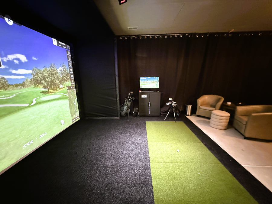 basement golf simulator with black turf and a cage