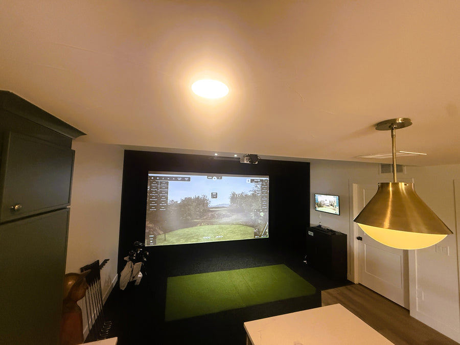 Indoor golf simulator setup in a room with a screen displaying a golf course.