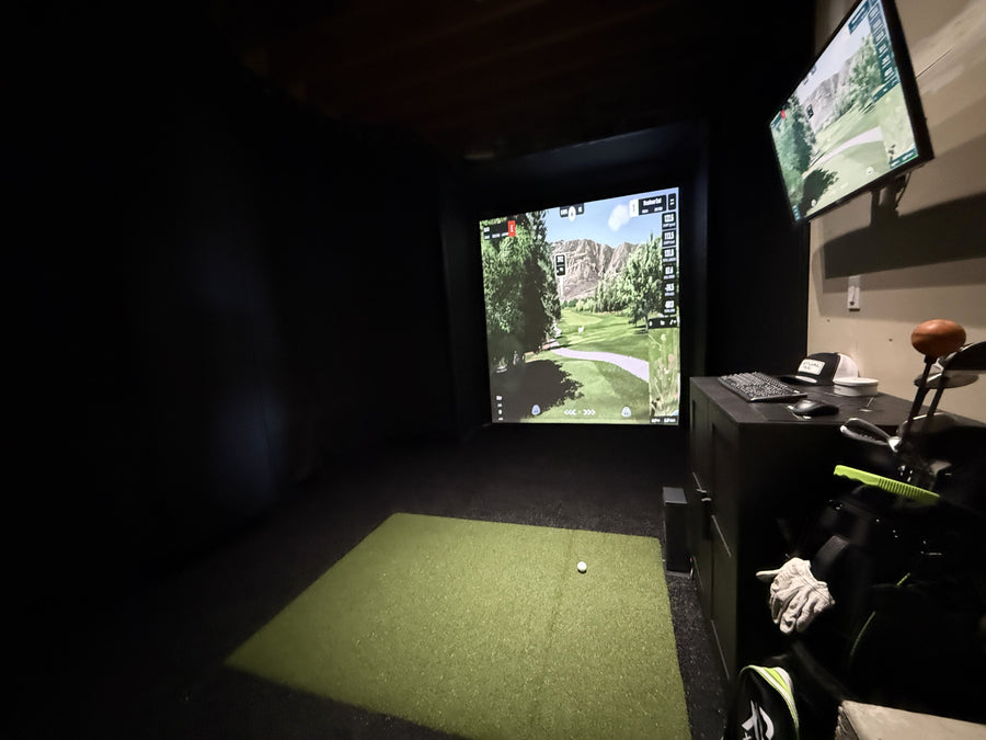 Indoor golf simulator setup with two screens displaying a golf course.