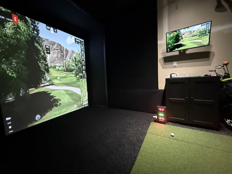 Golf simulator setup with two screens displaying a golf course in a dark room.