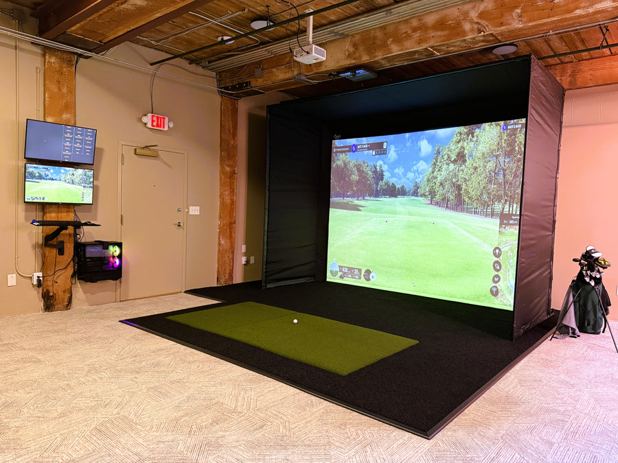 Golf simulator setup with large screen and practice mat in a room.