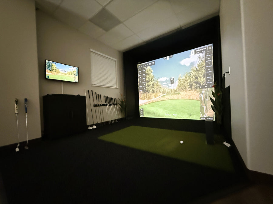 Indoor golf simulator setup with a monitor and big hitting screen displaying a golf course.