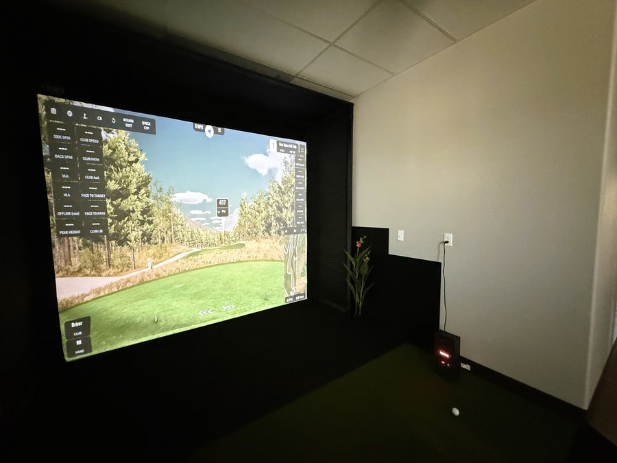 Indoor golf simulator setup with screen displaying a golf course.