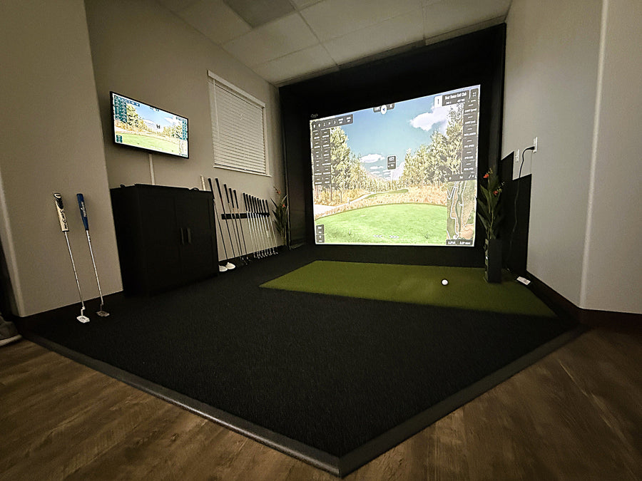 Golf simulator setup with two screens displaying a golf course, surrounded by golf clubs and equipment.