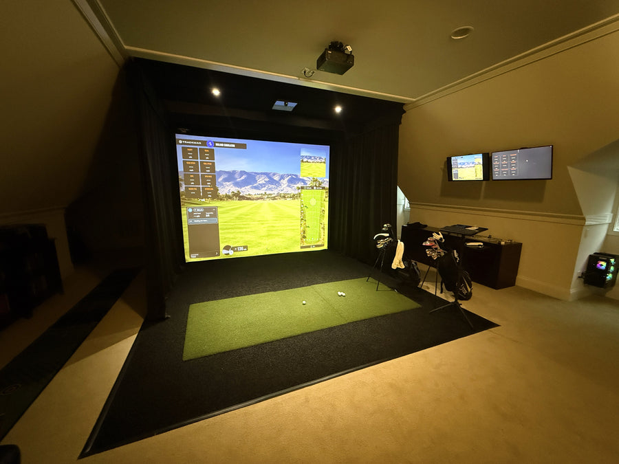 Indoor golf simulator setup with large screen and golf equipment in a room.