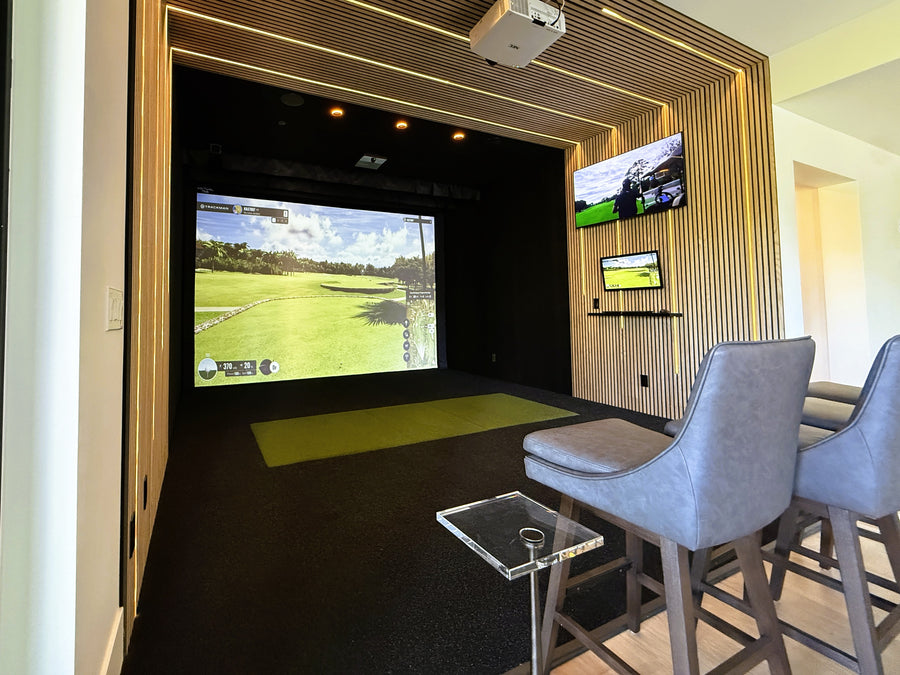 Indoor golf simulator setup with multiple screens and chairs in a modern room.