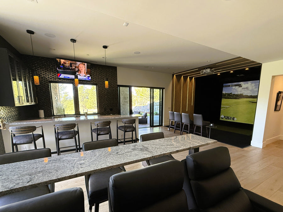 Modern living room with a large dining table, chairs, and a golf simulator room displaying a golf game.