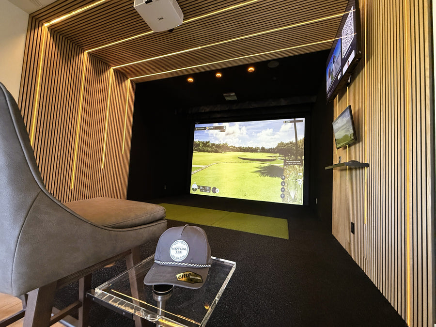 Indoor golf simulator setup with a screen displaying a golf course, surrounded by wooden paneling and a chair.