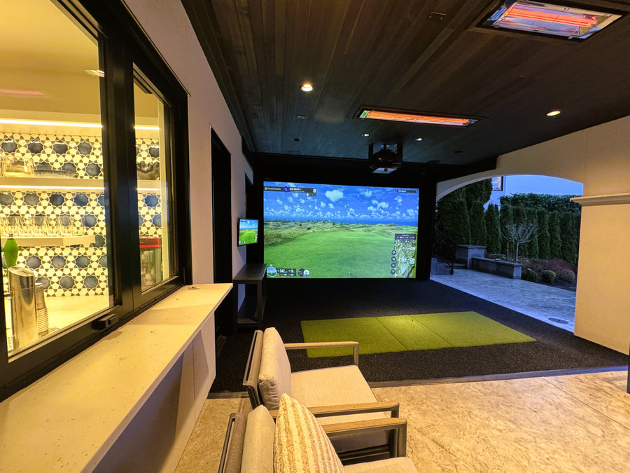 Outdoor golf simulator setup in a modern patio with a large screen displaying a golf course.
